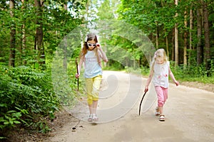 Two cute little sisters having fun during forest hike on beautiful summer day. Active family leisure with kids.