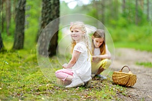 Two cute little sisters having fun during forest hike on beautiful summer day. Active family leisure with kids.