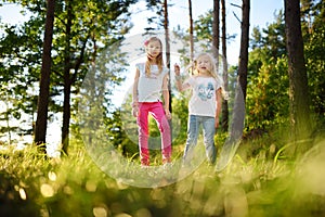 Two cute little sisters having fun during forest hike on beautiful summer day. Active family leisure with kids.