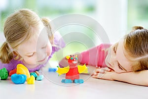 Two cute little sisters having fun together with colorful modeling clay at a daycare