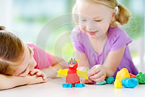 Two cute little sisters having fun together with colorful modeling clay at a daycare. Creative kids molding at home.