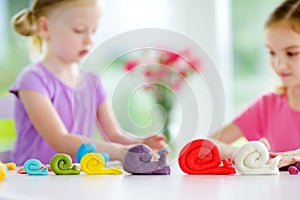 Two cute little sisters having fun together with colorful modeling clay at a daycare. Creative kids molding at home.