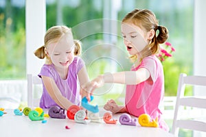 Two cute little sisters having fun together with modeling clay at a daycare. Creative kids molding at home. Children play with pla