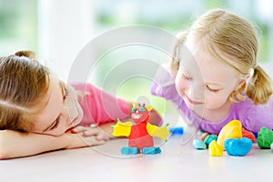 Two cute little sisters having fun together with modeling clay at a daycare. Creative kids molding at home. Children play with pla