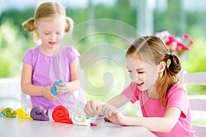 Two cute little sisters having fun together with modeling clay at a daycare. Creative kids molding at home. Children play with pla