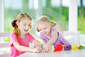 Two cute little sisters having fun together with modeling clay at a daycare. Creative kids molding at home. Children play with pla