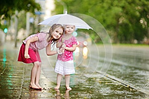 Two cute little sisters having fun under a rain