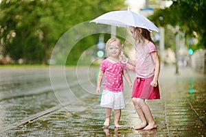 Two cute little sisters having fun under a rain