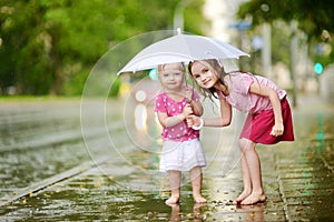 Two cute little sisters having fun under a rain