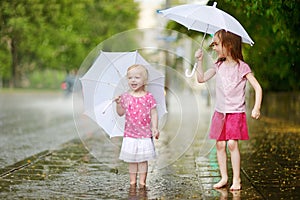 Two cute little sisters having fun under a rain