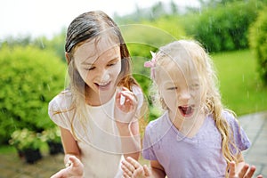 Two cute little sisters having fun under warm summer rain