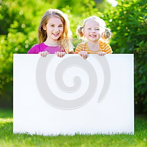 Two cute little sisters holding big blank whiteboard