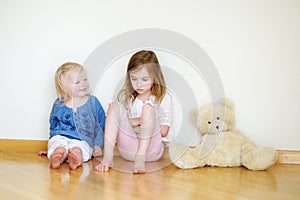Two cute little sisters sitting on a floor