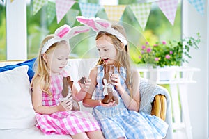 Two cute little sisters wearing bunny ears eating chocolate Easter rabbits