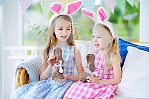 Two cute little sisters wearing bunny ears eating chocolate Easter rabbits