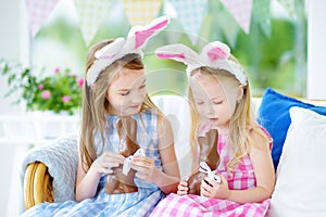 Two cute little sisters wearing bunny ears eating chocolate Easter rabbits