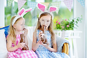 Two cute little sisters wearing bunny ears eating chocolate Easter rabbits