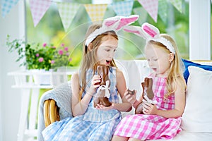 Two cute little sisters wearing bunny ears eating chocolate Easter rabbits