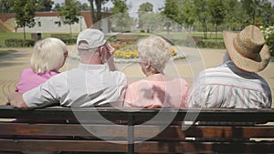 Two cute mature couples sitting on the bench and talking together. Mature people resting outdoors. Cheerful senior