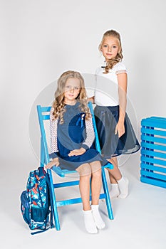 Two cute schoolgirls in a beautiful trendy school uniform with a backpack, books and notebooks with blue chair