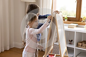 Two cute sibling kids drawing on toy small childish whiteboard