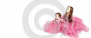 Two cute sisters in evening bright identical pink dresses on a white background with copy space