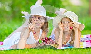 Two cute sisters or friends in a picnic garden lie on a deck and eat freshly picked cherries