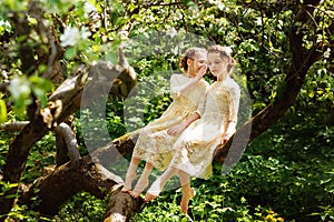Two cute sisters in matching dresses have fun in nature together in a beautiful summer garden on a warm and sunny day outdoors