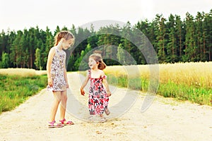 Two Cute sisters running on a green grassy field with smiles on their faces. Kids spending time together outdoor.