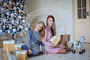 Two cute sisters sitting under Christmas tree