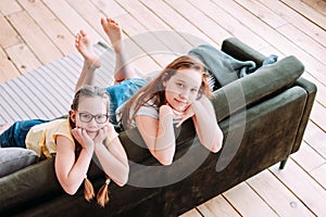 Two cute smiling girls children friends tweens sitting on sofa at home