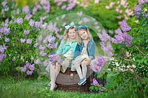Two cute smiling girls sisters lovely together on a lilac field bush all wearing stylish dresses and jeans coats.