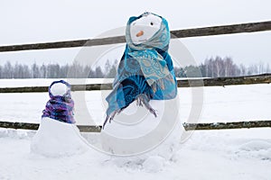 Two cute snowmen wrapped in scarves on snowy field.