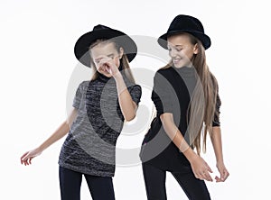 Two cute teenage girlfriends schoolgirls wearing turtleneck sweaters, jeans and hats, smiling dancing.  on white. Fashion