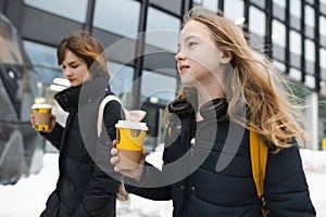 Two cute teenage girls with takeaway coffee cups on winter day. Teenager kids drinking hot beverage on chilly day
