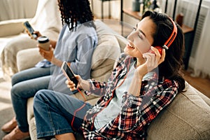 Two cute women in headphones leisures on sofa