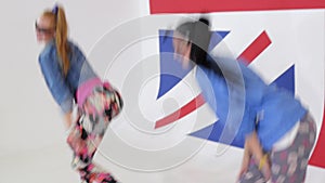 Two cute women in sunglasses practice synchronic dancing in studio with UK flag.