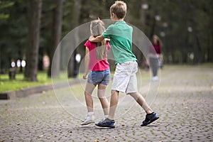 Two cute young laughing children, girl and boy, brother and sister having fun on blurred bright sunny summer park alley green