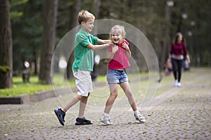 Two cute young laughing children, girl and boy, brother and sister having fun on blurred bright sunny summer park alley green