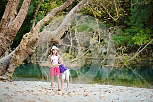 Two cute young sisters having fun by Voidomatis river on warm and sunny summer day during family vacations in Zagoria, Greece