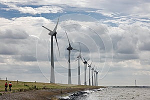 Two Cyclists at dike IJsselmeer near long row of windturbines