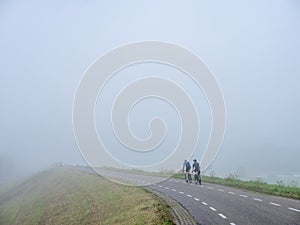 two cyclists on dike of river rhine in province of utrecht