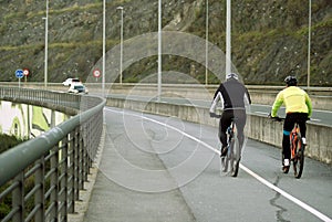 Two cyclists dressed for sport pedaling with cars near by