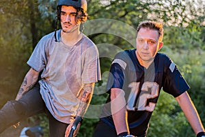 Two cyclists-friends, with bicycles, in the forest, against the setting sun