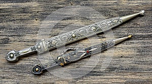 Two daggers with ornate pattern on old wooden background close-up.