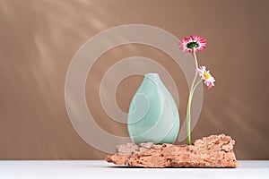 Two daisy spring flowers near a tiny green glass vase on brown