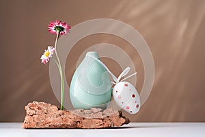 Two daisy spring flowers near a tiny green glass vase on brown photo