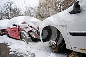 Two damaged cars covered with snow, sitting in front of each other in a line of broken cars, awaiting repairs