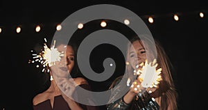 Two dancing girls laughing and smiling burn and waving sparklers celebrating for birthday and new year, Christmas