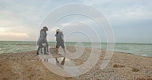 Two daring pirates walk away along the sandy seashore, led by their captain in tricorn hat and in wig with dreadlocks